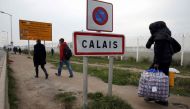 A migrant carries bags with his belongings as he walks past the Calais city limit sign on the eve of the evacuation and transfer of migrants to reception centers in France, and the dismantlement of the camp called the 