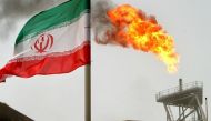 A gas flare on an oil production platform in the Soroush oil fields is seen alongside an Iranian flag in the Persian Gulf, Iran, July 25, 2005. REUTERS/Raheb Homavandi/File Photo.