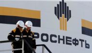 Workers stand next to a logo of Russia's Rosneft oil company at the central processing facility
