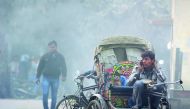 A rickshaw puller talks on his mobile phone as smoke emanates from garbage burning on a road in Allahabad, yesterday. 