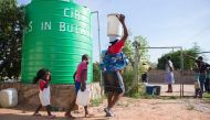 This file photo taken on November 24, 2016 shows a woman and her children carrying water cans, fetched from a tank installed at a church in Luveve on the outskirts of Bulawayo, Zimbabwe. From jobless youths hired to dig wells to illegal sellers supplying 