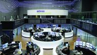 Traders work at their desks in front of the German share price index, DAX board, at the stock exchange in Frankfurt.
