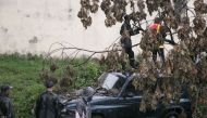 Malagasy firefighters work to remove a fallen tree from a car caused by tropical cyclone Enawo in Antananarivo, Madagascar, on March 8, 2017.  AFP / RIJASOLO
