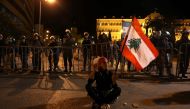 A Lebanese woman holding her national flag sits in the middle of the street as riot police guard the Grand Serail (the prime minister's headquarters) in downtown Beirut on March 16, 2017, during a protest against the Lebanese Parliament's newly approved t