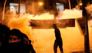 Anti riot police throws tear gas as a man stand next to a banner reading 