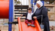 Hajar Saleh helps her grandson Jaafar playing on a slide inside a garden in the Damascus district of Mezzeh, Syria March 30, 2017. Picture taken March 30, 2017. REUTERS/Omar Sanadiki
