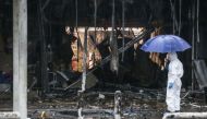 A Thai forensics worker shields himself with an umbrella whilst inspecting the aftermath of a bomb attack in the town centre of Pattani on May 9, 2017 (AFP Photo/TUWAEDANIYA MERINGING).