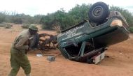 A picture taken with a mobile photo on May 25, 2017 shows a policeman looking at the wreckage of a police vehicle following a road side bomb in Garissa, northeastern Kenya.  AFP 
