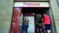A man operates at the ATM as customers exit a Banco Popular branch, yesterday, near Barcelona after European authorities announced the sale of the bank.