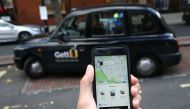 A woman poses holding a smartphone showing the App for ride-sharing cab service Uber in London on September 22, 2017. AFP / Daniel LEAL-OLIVAS

