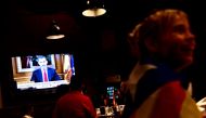 A woman wrapped in a Catalan pro-independence 'Estelada' flag listens to Spain's King Felipe VI address to the nation on a television set in a bar in Barcelona on October 3, 2017 during a general strike in Catalonia. AFP / PIERRE-PHILIPPE MARCOU