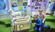 A picture taken on November 1, 2017 shows boys playing a game on a mobile phone next to the dog Laika's space container used for trainings ahead of blasting off to orbit the Earth on November 3, 1957, at the Central House of Aviation and Cosmonautics in M