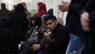 A Palestinian man holds a girl between his arms as he sits in a makeshift station in Khan Younis in the southern Gaza strip on November 18, 2017 as they await clearance to take a bus to travel through the Rafah border crossing with Egypt, after it opened 