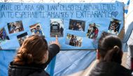 Women look at family pictures of missing Argentine submarine crew member Cesar Oscar Vallejos, hanging outside Argentina's Navy base in Mar del Plata, on the Atlantic coast south of Buenos Aires, on November 24, 2017. (AFP / EITAN ABRAMOVICH)