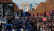 People gather during a 'popular homage' to late French singer Johnny Hallyday as his coffin is driven down the Champs-Elysees avenue on December 9, 2017 in Paris, with the Arc de Triomphe in the background.  AFP / Patrick KOVARIK
