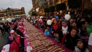People share balloons as they stand next to a massive cake known as 