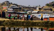 (FILES) This file photo taken on November 22, 2017, shows Rohingya refugees are reflected on a pond as they walk back to their homes at Balukhali refugee camp in the Bangladeshi district of Ukhia. AFP / Munir Uz Zaman 
