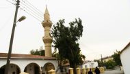 A couple walks past a mosque in the mixed village of Pyla, which lies in the UN-patrolled buffer zone that slices across the island of Cyprus. Clement Melki / AFP
