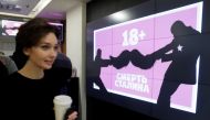 A woman walks past a monitor displaying the 