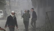 An elderly Syrian man carries a child as he walks through the dust following a reported regime air strike in the rebel-held town of Hamouria, in the besieged Eastern Ghouta region on the outskirts of the capital Damascus, on February 6, 2018. / AFP / ABDU