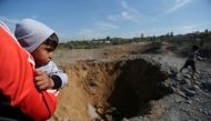 A Palestinian boy is carried as he looks at the scene of an Israeli air strike, south of Gaza City March 18, 2018. REUTERS/Ibraheem Abu Mustafa