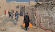 File photo of shows Afghan female labourer Sitara Wafadar, 18, who dresses as a male in order to support her family, collecting water near her home in Sultanpur village in Surkh Rod district, in Afghanistan's eastern Nangarhar province, March 20, 2018. / 