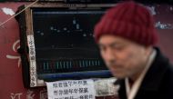 This picture taken on March 25, 2018 shows Shen Yuxi (R), who peddles stock analysis software, next to the screen of his computer showing financial data at Shanghai's open-air investment bazaar.  AFP / Johannes Eisele
