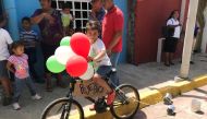 A child rides a bike adorned with balloons and a sign reading 