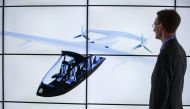 A man poses alongside screens presenting the Rolls-Royce EVTOL air taxi concept during the Farnborough Airshow, south west of London, on July 16, 2018. / AFP / Tolga AKMEN / 