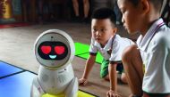 This photo taken on July 30, 2018 shows children watching a Keeko robot make its way on a path they made from square mats at the Yiswind Institute of Multicultural Education in Beijing. AFP / Greg Baker 