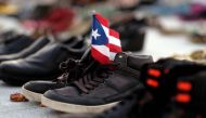 :(FILES) In this file photo taken on June 1, 2018 a view of a Puerto Rican flag placed on a pair of shoes among hundreds displayed in memory of those killed by Hurricane Maria in front of the Puerto Rican Capitol, in San Juan.  AFP / Ricardo ARDUENGO
