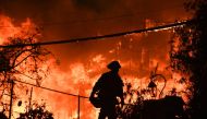 (FILES) In this file photo taken on November 9, 2018, a firefighter is silhouetted by a burning home along Pacific Coast Highway (Highway 1) during the Woolsey Fire in Malibu, California. AFP / Robyn Beck