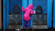 A migrant girl, part of a caravan of thousands from Central America trying to reach the United States, tries to avoid flooded ground by holding on to the door of a toilet after heavy rainfall in a temporary shelter in Tijuana, Mexico, November 29, 2018. R