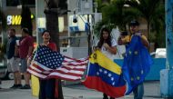 People holding the United States, Venezuelan and the European flag watch as a motorcade with US President Donald Trump travels from Mar-a-Lago to Trump International Golf Club for a Super Bowl party February 3, 2019 in West Palm Beach, Florida. / AFP / Br