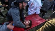 A Palestinian man carries an injured youth at the border fence with Israel east of Gaza City on March 22, 2019. AFP/Said Khatib 