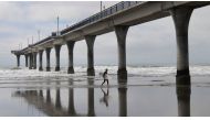 A surfer runs under the New Brighton Pier in Christchurch on March 24, 2019, as the city attempts to resume normal life after the shootings in local mosques. AFP / William West 
