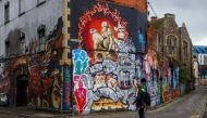 A pedestrian walks past graffiti street art on the side of a building in Bristol, south west England, on May 8, 2019.  AFP / Geoff Caddick 
