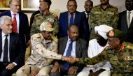 African union envoy to Sudan Mohamed al-Hacen Lebatt (L) sits next to Sudan's deputy chief of the ruling military council General Mohamed Hamdan Dagalo as he shakes hands with an army general following a press conference in Khartoum in which they announce