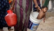A woman carries her son in a bucket after collecting water from a municipal water tanker on the outskirts of Chennai, India, July 4, 2019. (REUTERS/P. Ravikumar)