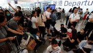 Passengers walk past anti-government protesters sitting on the floor in front of security gates during a demonstration at Hong Kong Airport, China August 13, 2019. REUTERS/Issei Kato