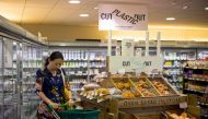 Signs promoting plastic free packaging are seen above a display of loose fresh fruit as a shopper browses at Budgens supermarket in Belsize Park, north London on July 2, 2019. AFP / TOLGA AKMEN 