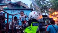 An Indonesian policeman helps evacuate a family as houses burn after hundreds of demonstrators marched near Papua's biggest city Jayapura on August 29, 2019. AFP / Indra Thamrin Hatta 