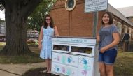 Amanda Santana (L) and Anna Rissi stand with their Little Free Pantry project in Alexandria, Virginia, in September 2019. Thomson Reuters Foundation/Carey L. Biron