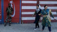 An Indian paramilitary trooper gestures as Kashmiri women walk past next to closed shops during a lockdown in Srinagar on October 23, 2019.  AFP / Tauseef Mustafa
 