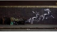 A man lays on a bench next to a new mural by Banksy in Birmingham, Britain, December 9, 2019, in this picture obtained from social media. @banksy/Instagram via Reuters 