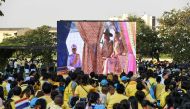 Spectators look at a gian screen showing Thailand's King Maha Vajiralongkorn, his wife Queen Suthida and Prince Dipangkorn Rasmijotion sitting at the Royal barge at the start of the Royal Barge procession, in Bangkok on December 12, 2019. The Royal barge 