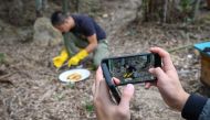 Chinese farmers Ma Gongzuo's assistant (pictured hands) using a mobile phone to take a video as Ma Gongzuo (C) tastes honey at his apiary in Songyang county in China's Zhejiang province on November 13, 2019. AFP / Wang Zhao