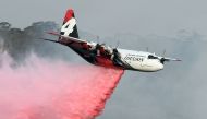 (FILES) This file photo taken on January 10, 2020 shows a C-130 Hercules plane from the New South Wales Rural Fire Service dropping fire retardent to protect a property during an operation to douse bushfires in Penrose, in Australia's New South Wales stat
