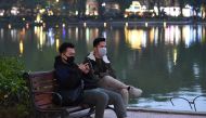 Two men wearing protective facemasks sit by the Hoan Kiem Lake in Hanoi on January 31, 2020. AFP / Nhac NGUYEN