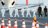 Workers and army officers wearing protective suits walk away from the cruise ship Diamond Princess, as they prepare to transfer passengers tested positive for the novel coronavirus, at Daikoku Pier Cruise Terminal in Yokohama, south of Tokyo, Japan Februa
